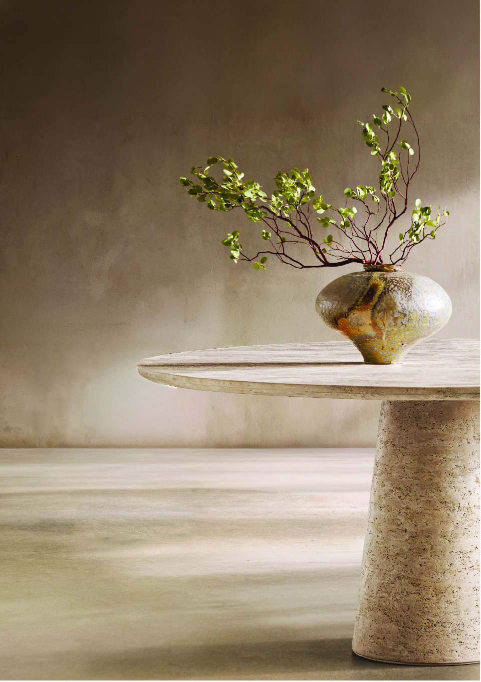 Sculptural ceramic vase with branches on a travertine pedestal table